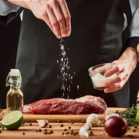 cocinero echando sal a un filete crudo sobre tabla de cortar